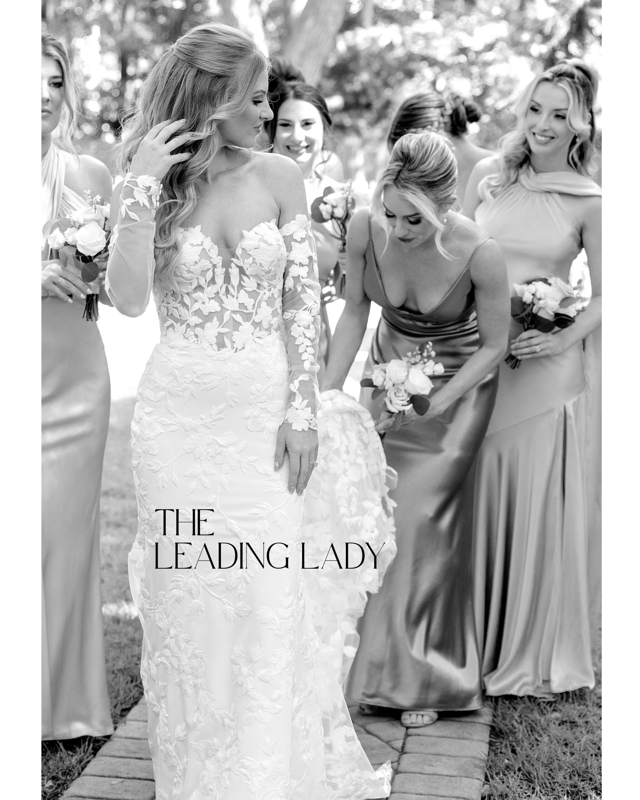 A bride surrounded by her bridesmaids that are holding her train and adjusting her dress
