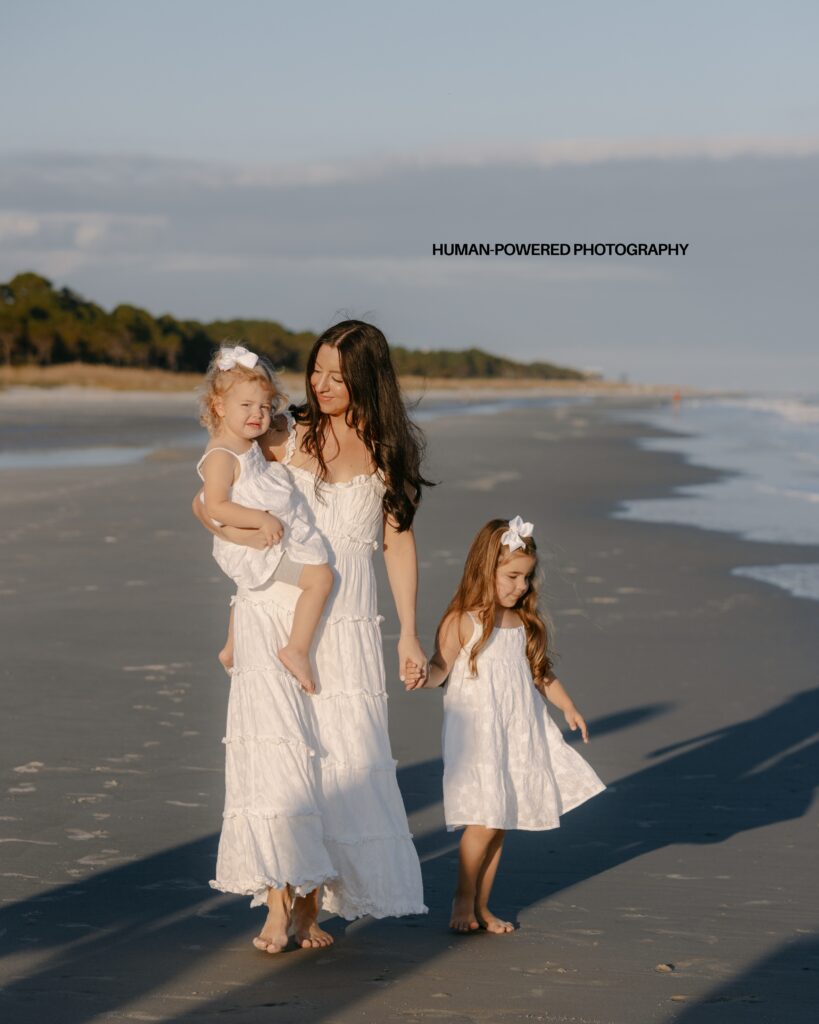 A mom and daughters on the beach in Hilton Head walking hand in hand during a photography session dressed all in white dresses