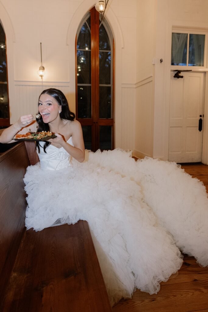 bride sitting in the chapel at Palmetto Bluff in a beautiful ruffled gown sitting in a pew eating some food
