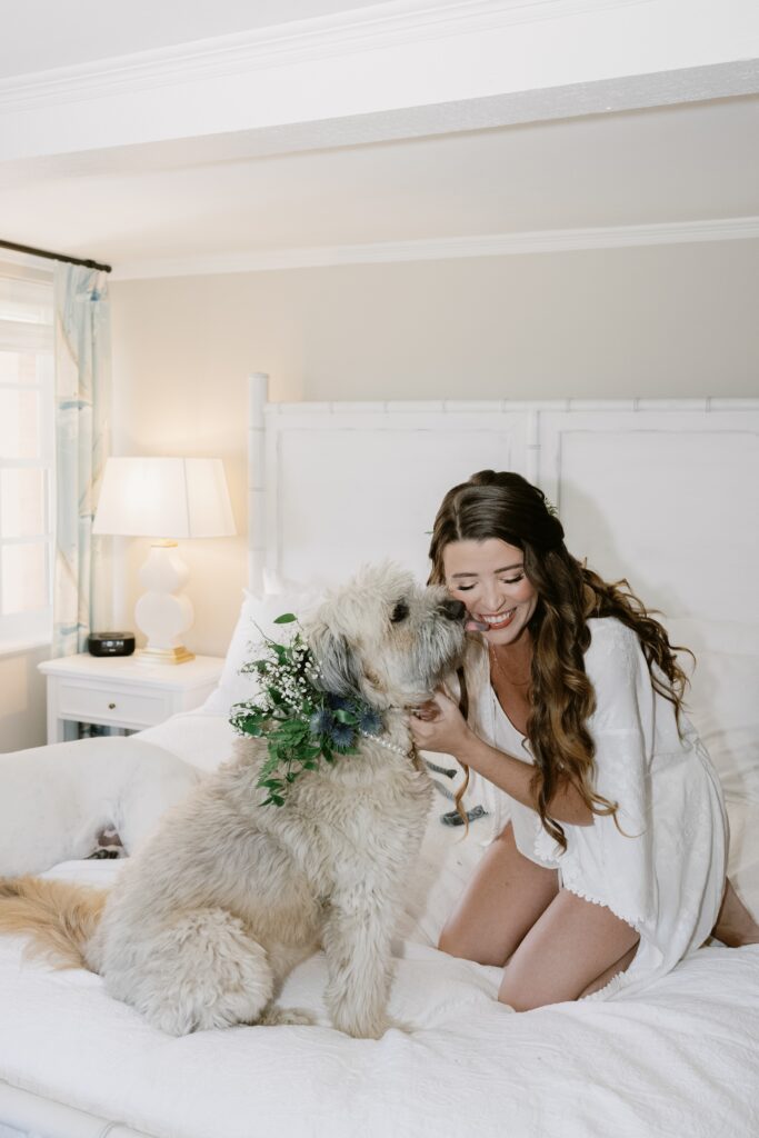 Bride getting ready at Cuthbert House Inn, Beaufort playing with her dog on the bed in her bridal pajamas