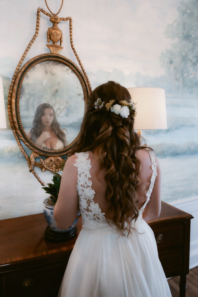 A bride looking in the mirro after getting her dress on at Cuthbert House Inn