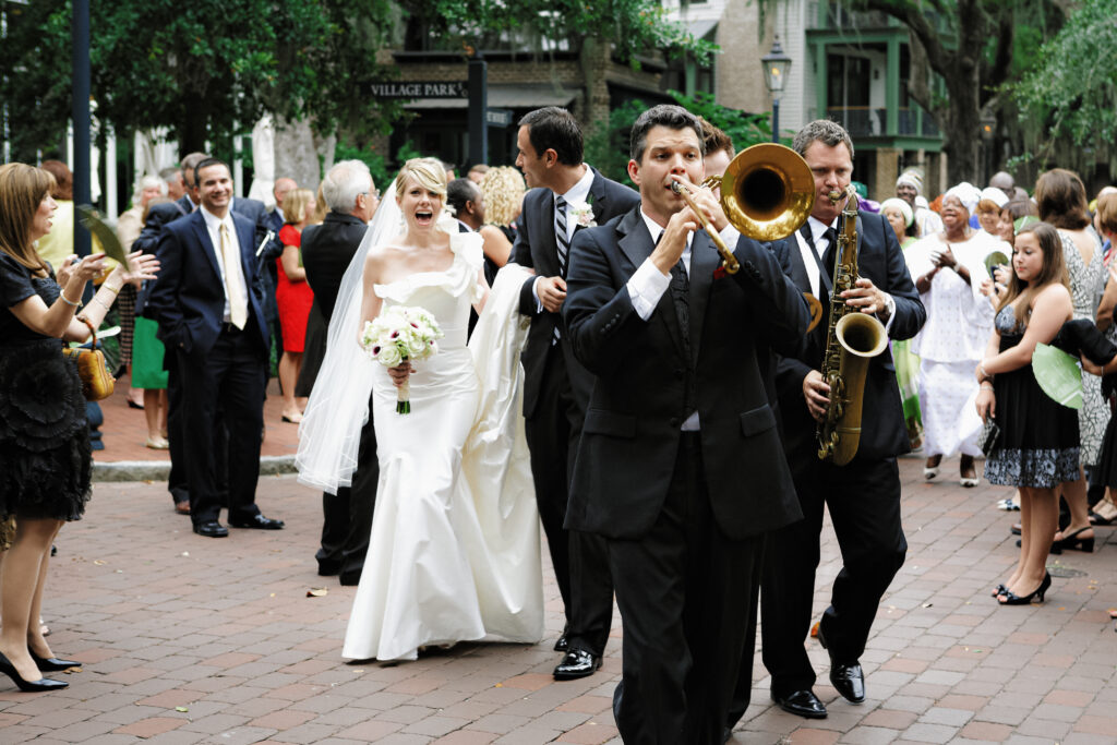 Bride and groom at Palmetto Bluff being lead by a New Orleans style band wearing tuxidos down the street